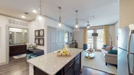This single-floor residence offers a thoughtfully designed open-concept layout that seamlessly connects the kitchen, dining, and living areas. The kitchen serves as the centerpiece, showcasing rich dark-wood cabinetry, a subway tile backsplash, stainless steel appliances, and a generously sized granite-topped island illuminated by stylish glass pendant lights. Hardwood-style flooring runs throughout the main living areas, adding warmth and continuity.

The living room is bright and inviting, benefiting from large sliding glass doors that open to a private balcony and frame outdoor views. Crown molding and recessed lighting contribute to a polished finish throughout.

The bedrooms feature plush carpeting, ceiling fans, and well-sized windows dressed with decorative curtains that allow ample natural light. Each bedroom includes access to a closet, providing practical storage. The bathroom is elongated and functional, featuring a dark-wood double vanity with granite countertops, hardwood-style flooring, a tub-shower combination, and a separate water closet. The overall design balances contemporary finishes with a comfortable, livable aesthetic.