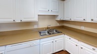This single-story space offers a practical and straightforward layout, as revealed by the 3D floor plan. The living area features wood-look flooring and connects seamlessly to a dining space accented by a candelabra-style chandelier. The kitchen is equipped with white raised-panel cabinetry, tan laminate countertops, a double-basin stainless steel sink, a white dishwasher, and a white range, providing functional workspace throughout.

Multiple bedrooms are finished with neutral-toned carpet and warm beige walls. Several rooms include ceiling fans with integrated light fixtures, while windows fitted with blinds or sheer curtains allow natural light and outdoor views. Textured ceilings are consistent throughout the space, and white baseboards provide clean visual contrast against the flooring.

Two full bathrooms are present, each featuring a tub/shower combo with a white surround, a toilet, and a vanity with white cabinetry and a tan countertop. Wood-look flooring runs through both bathrooms. The overall ambiance is clean, neutral, and move-in ready, with a cohesive color palette of beige, white, and warm wood tones maintained throughout.