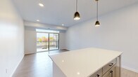 Located at 310 Third St in Farmington, MN, this well-appointed one-bedroom, one-bathroom unit offers a thoughtfully designed layout across a single floor. The open-concept kitchen and living area serves as the heart of the space, where light-toned luxury vinyl plank flooring, recessed lighting, and a pair of stylish gold-toned pendant lights create a warm, modern ambiance. The kitchen is fully equipped with stainless steel appliances — including a gas range, dishwasher, refrigerator, and microwave — complemented by gray shaker-style cabinetry, a white subway tile backsplash, quartz countertops, and a large central island ideal for dining or meal prep. The living area flows naturally toward a full-width sliding glass door that opens onto a private balcony, offering outdoor views and abundant natural light. The bedroom features plush carpeting, a closet, and a clean, neutral palette. A dedicated laundry room includes a stacked washer and dryer along with built-in wire shelving for added storage convenience. The bathroom is finished with a full soaking tub and shower combination. Throughout the unit, crisp white walls and consistent finishes contribute to a cohesive, contemporary aesthetic.