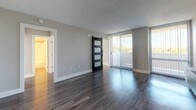 This thoughtfully renovated single-floor residence at 2000 Riverside Dr in Richmond, Virginia offers a clean, modern aesthetic throughout. The open layout is anchored by dark hardwood-style flooring in the main living area, which is bathed in natural light from large sliding glass doors that lead to an outdoor space. A striking black barn door with frosted glass panels serves as a stylish architectural focal point, adding a contemporary industrial touch to the living space.

The kitchen has been updated with white shaker-style cabinetry, speckled granite countertops, a stainless steel undermount sink with a brushed nickel pull-down faucet, and a glossy gray subway tile backsplash. A built-in dishwasher completes the functional layout.

The bedroom features lighter hardwood-style flooring, neutral gray walls, and a large window with blinds that bring in abundant natural light and outdoor views. A wall-mounted heating unit provides climate control.

The bathroom is finished in a clean, minimalist style with white cabinetry, brushed nickel hardware, a white vanity countertop, wood-look flooring, and a full tub-shower combination. Recessed lighting adds a polished touch. Overall, the space presents a cohesive, updated interior well-suited for comfortable everyday living.