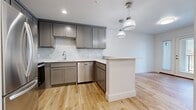 This thoughtfully designed one-bedroom, one-bathroom unit offers a modern and cohesive aesthetic across its single-floor layout. Light-toned hardwood flooring runs throughout the entire space, creating a warm, unified foundation that complements the clean, neutral color palette.

The open-concept kitchen and living area serves as the heart of the unit. The kitchen is well-appointed with gray shaker-style cabinetry, a classic subway tile backsplash, light quartz countertops, and a full suite of stainless steel appliances including a refrigerator, range, microwave, and dishwasher. A peninsula with a white countertop provides additional prep space and separates the kitchen from the living area, which is illuminated by stylish pendant lighting overhead.

The living area connects to a set of glass-paneled French doors that invite natural light and provide access to an outdoor space. The bedroom is a comfortable, well-lit room featuring a large window with outdoor views and a dedicated closet with built-in shelving and a hanging rod. The bathroom continues the gray cabinetry theme with a matching vanity, white countertop, and wood-look flooring. The space is clean, modern, and move-in ready.