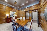 This distinguished single-floor space masterfully combines classical architectural elegance with practical, modern amenities. Rich hardwood flooring flows throughout, anchoring each area with warmth and continuity. Decorative fluted columns with Ionic capitals and detailed crown molding frame the transitions between spaces, lending a sense of grandeur to the overall layout.

The formal conference or dining room is a standout feature, fully clad in warm, raised-panel wood walling from floor to ceiling. A polished wood table surrounded by upholstered chairs sits beneath a striking multi-pendant chandelier, while a sunburst mirror adorns one wall and natural light filters in through windows dressed with linen drapes and wooden blinds, creating an atmosphere of refined sophistication.

Adjacent to the conference room, the business center is a well-appointed workspace featuring a continuous desk along one wall, three computer workstations with ergonomic seating, and decorative wall sconces illuminating a trio of framed botanical prints above — a thoughtful blend of productivity and aesthetic detail.

The open common area benefits from tall ceilings, crisp white millwork, and abundant natural light from large windows overlooking greenery. A built-in water fountain alcove and an accessible restroom with a classically trimmed doorframe reflect careful attention to practical needs. A glazed French door adds an additional architectural accent, completing this polished and functional space.