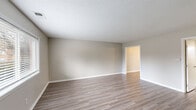 This two-story home presents a clean, neutral aesthetic throughout, with a consistent design language that emphasizes functionality and simplicity. The main living areas feature light wood-look laminate flooring paired with warm greige walls and crisp white trim, creating a bright and cohesive atmosphere. Textured ceilings add a subtle architectural detail present across multiple rooms.

The main level includes a generously sized open living area with a sliding glass door dressed in vertical blinds, allowing natural light to filter in while providing access to the outdoors. The kitchen is well-appointed with rich dark wood cabinetry, light granite-style countertops, and black appliances including a refrigerator, electric range, and over-the-range microwave. A window above the sink adds natural light to the workspace.

Adjacent living and transitional spaces are connected by open doorways, facilitating a smooth flow between rooms. A full bathroom on this level features a dark wood vanity, a decoratively framed mirror, and louvered bifold closet doors for added storage.

Upper-level rooms are carpeted in a warm neutral tone, offering a softer feel suited for bedrooms. Windows throughout provide outdoor views and natural light, enhancing the overall livability of the space.
