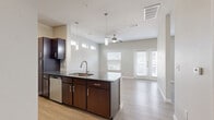 Located at 7210 Potranco Road in San Antonio, Texas, this one-bedroom, one-bathroom unit offers a thoughtfully designed single-floor layout that maximizes every square foot. Light-toned wood-look flooring flows consistently throughout the space, creating a cohesive and clean aesthetic.

The kitchen is a standout feature, equipped with stainless steel appliances including an electric range, over-the-range microwave, and dishwasher. Rich dark-brown cabinetry with brushed nickel hardware contrasts elegantly with dark granite-style countertops. A central island with a stainless steel sink and pendant lighting above connects the kitchen to the open living area, where large windows and French doors flood the room with natural light. A ceiling fan adds to the living room's comfort, and the French doors lead directly to a private patio.

The bedroom offers a comfortable footprint with its own ceiling fan, high walls, and direct access to a dedicated walk-in closet with built-in shelving. The full bathroom features a framed glass-enclosed shower, a dark-cabinet vanity with a stone-top sink, and matching wood-look tile flooring. Clean white millwork and neutral wall tones throughout the unit contribute to a bright, modern ambiance well-suited for efficient, comfortable living.