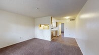 Located at 600 N Pantano Rd in Tucson, Arizona, this single-floor unit offers a practical and functional layout designed for comfortable everyday living. The spacious living area is finished with plush wall-to-wall carpeting and neutral cream-toned walls, creating a warm and inviting atmosphere. A textured ceiling runs throughout the space, adding a classic residential character. Natural light filters in through a front door with a sidelite window, brightening the entry and living zone.

The kitchen is separated from the living area by a half-wall partition featuring a convenient pass-through window, allowing for easy interaction between spaces. The kitchen is equipped with cabinetry, a range, and essential appliances, with wood-look flooring that extends into the connecting hallway. This transition from carpet to hard-surface flooring clearly delineates the living and functional zones of the unit.

The bedroom is a generously sized, carpeted room with a window dressed with blinds, allowing for controlled natural light and privacy. The bathroom features a well-lit vanity with a large mirror, built-in storage drawers, and wood-look flooring, offering a clean and efficient design. Overall, the unit presents a straightforward, move-in-ready space in a convenient Tucson location.