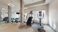 Located at 646 W Smith St in Orlando, FL, this well-appointed fitness center offers a comprehensive workout environment designed with both function and aesthetics in mind. The single-floor space is defined by its striking hexagonal-patterned flooring in neutral tones accented with teal, lending a modern, energetic feel throughout. Distinctive stone-clad structural columns add a warm, textural contrast to the otherwise sleek, contemporary interior.

The cardio zone is generously equipped with multiple treadmills, stair climbers, and elliptical machines, all positioned along large windows that flood the space with natural light and provide views to the outdoors. Overhead, geometric square LED light fixtures illuminate the space evenly, complementing the bright, airy atmosphere.

The strength training area features a robust selection of TKO cable and resistance machines, a free-weight section with a full dumbbell rack, a flat bench, and wall-length mirrors that enhance the sense of space. A dedicated entry zone includes sanitation stations, equipment-cleaning supplies, and open cubbies for personal belongings, ensuring a clean and organized environment.

Glass-paned double doors provide easy access, while the open floor plan allows for fluid movement between workout zones, making this fitness center a well-rounded facility for all training needs.