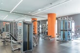 Located at 40 Lagerfeld Dr in Brampton, Ontario, this well-appointed fitness facility offers a comprehensive workout environment designed to inspire and perform. The space is laid out on a single floor and provides ample room for a diverse range of exercise equipment and activities.

The interior design strikes a bold visual identity, combining a neutral grey and white color palette with energetic orange accents — most notably on a signature cylindrical column and prominent motivational wall graphics, including a Muhammad Ali quote: "Don't count the days, make the days count." Large floor-to-ceiling windows line one wall, flooding the space with natural light and offering views of the surrounding Brampton neighborhood.

The facility is comprehensively equipped with Matrix-brand strength machines, a functional cable trainer, free weights with a dedicated dumbbell rack, and multiple cardio machines including treadmills, ellipticals, and stationary bikes. Full-length mirrors along one wall visually expand the space and support proper form during workouts.

Underfoot, large-format grey tile flooring provides a durable, clean surface throughout. Recessed pot lights and sleek linear LED fixtures illuminate the space evenly, complementing the modern architectural finishes. The overall ambiance is professional, energizing, and purpose-built for fitness.