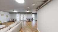 Located at 5764 Stevens Forest Rd in Columbia, MD, this single-floor community lounge offers a well-appointed gathering space designed for both relaxation and recreation. The room is unified by striking herringbone-patterned hardwood flooring that runs throughout, lending warmth and visual interest to the entire space.

The lounge is organized into several distinct functional areas. A comfortable seating zone anchors one end of the room, featuring a curved sectional sofa paired with a marble-top oval coffee table and accent chairs set against a rich, wood-slatted feature wall that adds texture and a modern mid-century aesthetic. A wall-mounted flat-screen television serves this area as well.

The recreation area is highlighted by a full-size billiards table and an additional wall-mounted TV, offering entertainment options for guests. Nearby, a sleek wet bar is outfitted with rich walnut cabinetry, a mosaic tile backsplash, a black sink fixture, and a built-in beverage refrigerator — ideal for hosting gatherings.

Multiple bistro-style tables and chairs are arranged throughout the space, providing casual spots for conversation or small group meetings. French doors along the perimeter invite natural light and provide direct access to the outdoor surroundings. The overall ambiance is clean, modern, and inviting, making this lounge a versatile and well-designed communal amenity.
