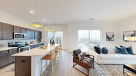 This contemporary single-floor residence is thoughtfully designed with a clean, modern aesthetic throughout. The open-concept kitchen and living area serves as the heart of the home, where dark, rich cabinetry pairs with white quartz countertops and a classic subway tile backsplash. Stainless steel appliances, including a range and built-in microwave, lend a polished, functional quality to the kitchen. A spacious island with bar seating and stylish pendant lighting makes the space ideal for both cooking and entertaining. The living area is bathed in natural light from oversized windows that frame expansive views of the surrounding neighborhood, creating a bright and airy atmosphere. Light wood-style flooring flows seamlessly through the main living spaces. The primary bedroom offers a serene retreat with plush carpeting, elevated ceilings, ample room for furnishings, and a window that brings in additional natural light. A second bedroom mirrors this comfortable simplicity. Two full bathrooms, each featuring tub-shower combinations, clean white finishes, and modern fixtures, serve the residence with ease. A dedicated office space provides a quiet area for work or study, complete with neutral tones and room for a full desk setup. Throughout, the residence maintains a cohesive, contemporary feel defined by light walls, clean lines, and a bright, welcoming ambiance.