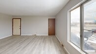 Located at 4979 S Washington Rd in Saginaw, Michigan, this two-bedroom, one-bathroom unit offers a practical and comfortable single-floor layout. The open living and dining area is finished with light hardwood-style flooring and neutral gray walls, creating a bright and airy atmosphere. Large windows allow natural light to flow throughout, enhancing the clean, understated aesthetic. The living space connects seamlessly to the combined dining and kitchen area, which features warm wood cabinetry, a marble-style countertop, a double sink, and white appliances including a range and refrigerator. A hallway leads to the two carpeted bedrooms, each finished with neutral tones and ceiling light fixtures. The primary bedroom is a comfortable size and includes direct access to a private balcony through a sliding glass door, offering views of the open surrounding landscape. The second bedroom features a built-in closet with louvered bifold doors. Both bedrooms benefit from natural light through windows. The full bathroom includes a vanity with white cabinetry, a tub/shower combination, and light hardwood-style flooring. Additional storage is provided by two closets accessible from the hallway. The balcony extends the living space outdoors, overlooking an expansive open field.