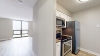 Located at 2555 N Clark St in Chicago's vibrant Lincoln Park neighborhood, this efficiently designed unit offers a well-planned layout across a single floor, comprising a living room, kitchen, bathroom, and hallway. The living area is a standout space, anchored by a large floor-to-ceiling window that frames sweeping city views and floods the room with natural light. Light-toned hardwood flooring runs throughout, complementing the neutral gray walls and textured ceiling to create a clean, modern aesthetic. A built-in closet with sleek panel doors provides generous storage, keeping the space organized and uncluttered. The kitchen is thoughtfully appointed with white shaker-style cabinetry, stainless steel appliances including a refrigerator, electric range, and over-the-range microwave, along with warm-toned countertops. Light hardwood flooring continues seamlessly into the kitchen, maintaining visual cohesion. The bathroom features white cabinetry with a dark countertop, an undermount sink, a framed mirror, and tile flooring, offering a tidy and functional layout. A connecting hallway ties the rooms together efficiently. Overall, the unit delivers a bright, contemporary feel with practical finishes suited for urban living in one of Chicago's most sought-after neighborhoods.