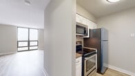 Located at 2555 N Clark St in Chicago's vibrant Lincoln Park neighborhood, this efficiently designed unit offers a well-planned layout across a single floor, comprising a living room, kitchen, bathroom, and hallway. The living area is a standout space, anchored by a large floor-to-ceiling window that frames sweeping city views and floods the room with natural light. Light-toned hardwood flooring runs throughout, complementing the neutral gray walls and textured ceiling to create a clean, modern aesthetic. A built-in closet with sleek panel doors provides generous storage, keeping the space organized and uncluttered. The kitchen is thoughtfully appointed with white shaker-style cabinetry, stainless steel appliances including a refrigerator, electric range, and over-the-range microwave, along with warm-toned countertops. Light hardwood flooring continues seamlessly into the kitchen, maintaining visual cohesion. The bathroom features white cabinetry with a dark countertop, an undermount sink, a framed mirror, and tile flooring, offering a tidy and functional layout. A connecting hallway ties the rooms together efficiently. Overall, the unit delivers a bright, contemporary feel with practical finishes suited for urban living in one of Chicago's most sought-after neighborhoods.