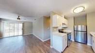 This single-floor residence in Suisun City, California (94585) offers a clean, modern interior with a thoughtfully designed layout. The galley-style kitchen is a standout feature, boasting crisp white shaker cabinetry, light marble-look countertops, stainless steel appliances including a range and refrigerator, and wood-look luxury vinyl plank flooring that extends throughout the main living areas. The kitchen opens toward a spacious living area illuminated by natural light from a sliding glass door that leads to the outdoors, and a ceiling fan adds both function and comfort overhead. A second living or dining area near the entry is equally well-lit and flows seamlessly from the kitchen. The bedrooms are finished with plush wall-to-wall carpeting and feature windows that frame views of surrounding greenery, lending a calm, natural ambiance to each room. The full bathroom is outfitted with a white tub and shower combination, a white vanity with marble-look countertop, and wood-look flooring that ties the space together cohesively. Neutral warm-gray wall tones throughout create a versatile backdrop, while consistent white trim and modern fixtures contribute to a polished, move-in-ready aesthetic across the entire unit.