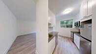 Located at 611 Woodbine Ave in Toronto's desirable East End neighbourhood, this thoughtfully renovated one-bedroom, one-bathroom unit offers a clean, modern aesthetic throughout its single floor. Light-toned hardwood-style flooring runs continuously through the space, creating a cohesive and airy feel.

The kitchen is a standout feature, showcasing white shaker-style cabinetry, dark countertops, and a classic subway tile backsplash. Stainless steel appliances — including a range, over-the-range microwave, and refrigerator — complete the well-appointed cooking space. A window above the kitchen area frames a lush, green outdoor view, filling the room with natural light.

The living area is open and versatile, offering a blank canvas for various furniture arrangements. The bedroom is a comfortable size, featuring soft neutral walls, light flooring, a classic cast iron radiator, and a window with a serene view of surrounding greenery — providing both natural light and a peaceful ambiance. Clean white panel doors connect the rooms with a tidy, consistent design.

The bathroom features a full soaking tub enclosed by crisp white subway tiles and chrome fixtures, lending a timeless, polished look. Throughout the unit, the bright white walls and natural light create a welcoming, move-in ready environment well-suited to those seeking a stylish home in Toronto's vibrant East End.