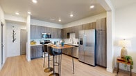 This thoughtfully designed 1-bedroom, 1-bathroom residence features a modern open-concept layout that maximizes its efficient footprint. Light wood-tone flooring flows seamlessly throughout the main living areas, creating a bright and cohesive aesthetic.

The kitchen is a standout feature, showcasing floor-to-ceiling wood-grain cabinetry, white quartz countertops, and a full suite of stainless steel appliances including a French door refrigerator with water dispenser, electric range with microwave, and dishwasher. A compact bistro-style dining table with bar seating provides a casual dining option within the kitchen space.

The open living area connects directly to the kitchen and offers recessed lighting, a wall-mounted flat-screen TV setup, and a wall-mounted mini-split HVAC unit for individual climate control. Natural light enters through a window fitted with horizontal blinds and sheer curtains.

The bedroom is a quiet, carpeted retreat featuring corner windows that allow ample natural light, sheer curtains, and its own wall-mounted mini-split unit for personalized comfort.

The bathroom is finished with the same wood-grain cabinetry as the kitchen, a white quartz vanity top, a large mirror, and a shower-tub combination. A hallway connects all rooms, completing this clean and functional single-floor layout.