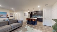 This well-appointed single-floor residence offers a thoughtfully designed open-concept layout that seamlessly connects the kitchen, dining, and living areas. The kitchen stands out as a centerpiece of the space, featuring dark espresso shaker-style cabinetry extending to the ceiling, a cool blue tile backsplash, stainless steel appliances, white quartz countertops, and a large island with an undermount sink and seating for multiple bar stools illuminated by sleek pendant lighting. The living area provides a comfortable, light-filled retreat with wood-look plank flooring, a ceiling fan, and a window that invites natural light. Two carpeted bedrooms offer a quiet escape, each equipped with ceiling fans and closet storage. One bedroom includes a spacious walk-in closet with dual hanging rods, while the other features a standard reach-in closet. The bathroom is finished with large-format tile flooring, dark cabinetry vanity, and a shower-tub combination. A dedicated in-unit laundry room houses a full-size washer and dryer beneath dark upper cabinetry, adding everyday convenience. Neutral tones, recessed lighting, and consistent finishes throughout create a cohesive, modern ambiance across the entire residence.