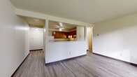This single-floor unit features a practical and functional layout designed to maximize the use of space throughout. The open-concept living area is finished with durable hardwood-style flooring in a cool gray tone, which flows consistently through the main living spaces. A defining architectural element is the half-wall partition that separates the living room from the kitchen, creating a pass-through effect that maintains an open and connected feel between the two areas. The living room receives natural light through a window offering exterior views, and baseboard heating units are positioned along the walls.

The kitchen is well-appointed with rich, warm-toned wood cabinetry extending to the upper and lower walls, providing ample storage. Countertops are light-colored and functional, complemented by a double basin sink, a gas range with an overhead ventilation hood, and a dishwasher. Hardwood-style flooring continues into the kitchen, maintaining visual consistency.

The bedroom is a generously sized room featuring a large built-in closet with wood-paneled sliding doors and brass hardware, a window bringing in natural light, and baseboard heating.

The bathroom includes a full tub-shower combo with a white surround, a vanity with wood cabinetry, and tile-style flooring, completing this well-organized and functional living space.