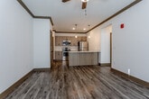 Located at 15201 NW Brink-Myer Rd in Parkville, Missouri, this single-floor unit offers a thoughtfully designed layout with contemporary finishes throughout. The open-concept kitchen and living area serves as the heart of the space, showcasing warm-toned, wood-look luxury vinyl plank flooring, rich crown molding, and a ceiling fan that enhances airflow and comfort. The kitchen is well-appointed with light wood cabinetry, stainless steel appliances including a range, microwave, and refrigerator, and a center island featuring a quartz countertop with an integrated sink — ideal for both meal preparation and casual dining. Pendant lighting above the island adds a modern touch, complementing the recessed lighting throughout. The entry area features warm-toned panel doors and seamlessly connects to the main living spaces. The bedrooms offer plush carpeting, large windows with blinds that invite generous natural light, and ceiling fans for added comfort. Two full bathrooms mirror the home's consistent design language, each featuring wood-look flooring, light wood vanities with quartz countertops, and tub-shower combinations. Clean white walls and cohesive brown trim details tie the entire space together, creating a modern yet welcoming atmosphere.