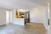 This single-story residence is designed with a practical, open-concept layout that connects the living area directly to the kitchen, creating a cohesive and functional main living space. The living area features wood-style luxury vinyl flooring in a light gray tone, complemented by neutral beige walls and a textured ceiling throughout.

The kitchen is positioned behind a peninsula-style island with a white countertop and gray cabinetry, offering both prep space and a casual seating area. It is equipped with a full suite of stainless steel appliances, including a refrigerator, microwave, and gas range. Gray shaker-style upper and lower cabinets provide ample storage. A dedicated laundry area with a washer is accessible directly from the kitchen.

The bedrooms feature soft carpeting and are well-lit by multiple windows with horizontal blinds, allowing natural light and outdoor views of greenery. Closet space is provided via louvered bifold doors with built-in shelving and hanging rods.

The bathrooms maintain a consistent design palette, each featuring a gray vanity with a white countertop, a framed mirror, and a combination tub and shower. Wood-style tile flooring ties the bathrooms cohesively to the rest of the unit's aesthetic.