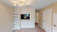 Located at 2825 Parkview Ln in Bedford, Texas, this two-story residence offers a functional and comfortable layout spread across two levels. The living area is finished with plush carpeting and features a built-in wall of white open shelving, providing practical display and storage space. A pass-through window connects the living area to the kitchen, creating an open, communicative flow between the two spaces. The kitchen is equipped with dark espresso cabinetry, light stone-finish countertops, and black appliances including a refrigerator, electric range, and over-the-range microwave, all set atop warm wood-tone flooring. The bedrooms are carpeted and bathed in natural light through blinded windows, each outfitted with ceiling fans fitted with light fixtures. The primary bedroom benefits from vaulted ceilings and dual windows that enhance the sense of openness. Bathrooms include a full tub-shower combination with white tile surround, as well as a vanity with dark cabinetry, a single-basin sink, stone-finish countertops, and a large mirror with brushed nickel lighting above. Throughout the home, warm beige tones and textured ceilings create a cohesive, neutral palette. The overall layout is well-organized, with clear transitions between living, dining, and private spaces.