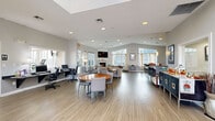 Located at 1420 Key Pkwy in Frederick, MD, this Westminster community clubhouse offers a generously proportioned, single-floor gathering space designed for both comfort and functionality. Residents are welcomed through a dramatic arched glass entryway that sets an inviting tone and fills the foyer with natural light.

The open-plan interior is anchored by light wood-look flooring that flows throughout, unifying the various activity zones. The main living area features a stone fireplace with a wall-mounted TV above, flanked by large windows that bathe the seating area in abundant natural light and offer views of the surrounding community. Comfortable lounge chairs and tasteful décor create a warm, residential ambiance.

Adjacent to the lounge, a full kitchen with stainless steel appliances, white cabinetry, and a large island with bar seating provides an ideal space for community gatherings and events. A dining area with round tables and cushioned chairs sits nearby for casual meals or group activities.

A dedicated business center with workstations and computers offers a productive workspace for residents. French doors lead to a separate game or activity room, providing additional flexible space. Recessed lighting throughout ensures a bright, welcoming atmosphere, while the vaulted ceiling transitions add architectural interest. This thoughtfully designed clubhouse serves as a true hub of community life.