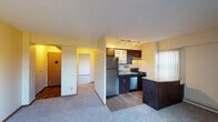 This single-floor residence offers a well-organized layout that balances living, sleeping, and functional spaces. The kitchen is a standout feature, showcasing dark wood cabinetry with frosted glass inserts, granite countertops, a curved peninsula island, stainless steel appliances including a refrigerator, gas range, and dishwasher, and hardwood-style flooring beneath track lighting. Vertical blinds on a nearby window allow for adjustable natural light.

The living area is generously sized, finished with plush wall-to-wall carpeting and warm yellow-toned walls, and connects openly to the kitchen via a partial dividing wall. The bedroom is a comfortable, carpeted room featuring a wide mirrored sliding-door closet with built-in shelving, providing ample storage. Large windows throughout the unit frame outdoor views of surrounding trees and neighboring buildings, while baseboard heating units and a wall-mounted air conditioner ensure year-round climate control.

The bathroom features white tile flooring, a wood vanity with under-shelf storage, a mirrored medicine cabinet, a sliding-door tub/shower enclosure, and a window that brings in natural light. Textured ceilings are consistent throughout the unit.