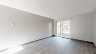 This single-floor unit at 17966 NE Oregon St in Gresham, Oregon, offers a clean, understated aesthetic throughout its layout. The living area is a standout feature, characterized by light-toned vinyl plank flooring, neutral gray walls, and a textured ceiling. A sliding glass door draws in generous natural light and provides a view of mature trees outside, creating a calm, connected atmosphere.

The kitchen is designed for functionality, featuring white cabinetry, a stainless steel sink, and white appliances including a range and refrigerator. Light vinyl flooring continues from the living area into the kitchen, maintaining a cohesive look. The galley-style layout makes efficient use of the available space.

The bedroom offers a quieter, more private feel with soft carpeting underfoot, neutral gray walls, a window with vertical blinds allowing filtered natural light, and baseboard heating. A closet with a standard door provides convenient storage.

The bathroom is neatly appointed with wood-look vinyl flooring, a vanity with storage, a toilet, and a shower-tub combination with a curved curtain rod. The overall palette throughout the unit is neutral and consistent, lending the space a clean, move-in ready quality.