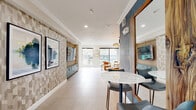 Located at 320 Jackson Hill St in Houston's vibrant 77007 corridor, this thoughtfully designed amenity lounge offers a generously proportioned, single-level space that seamlessly blends comfort, entertainment, and modern style. Light-toned porcelain tile flooring runs throughout, lending a clean and cohesive foundation to the interior.

The space is organized into distinct functional zones. A bold media wall, featuring vertical wood slat detailing and a built-in large-screen TV flanked by geometric-patterned wallcovering and teal-finished cabinetry, anchors the central area. Adjacent to this is a dedicated game room, equipped with a shuffleboard table and foosball table, lined with expansive floor-to-ceiling windows that flood the area with natural light and provide views of the surrounding outdoor spaces.

A cozy lounge nook is wrapped in striking blue botanical wallpaper and furnished with a plush sectional sofa, an artisan chandelier, and curated wall art, creating an intimate retreat within the larger space. Nearby, a seating area with sculptural accent chairs overlooks the pool area through large sliding glass doors.

The kitchenette is well-appointed with teal cabinetry, white quartz countertops, open floating shelves, a stainless steel sink, a compact refrigerator, and a microwave — complemented by a bold steel-framed window with outdoor views. Crown molding and recessed lighting throughout add refined architectural detail to this inviting communal space.