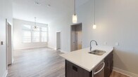 This well-appointed single-floor residence showcases a thoughtfully designed open-concept layout that seamlessly connects the kitchen, dining, and living areas. Soaring ceilings amplify the sense of space, while large windows fitted with blinds invite an abundance of natural light throughout. The living area features light-toned hardwood-style flooring and a ceiling fan, with a glass door providing additional outdoor access.

The contemporary kitchen is a standout, equipped with dark espresso cabinetry extending to ceiling height, white quartz countertops, a subway tile backsplash, and a full suite of stainless steel appliances including a French door refrigerator, range, microwave, and dishwasher. A peninsula with a double undermount sink and pendant lighting serves as both a functional workspace and a natural gathering point.

The bedrooms are carpeted for comfort, each featuring ceiling fans and generous window coverage for natural light. Both bathrooms are finished with dark wood cabinetry, white quartz vanity tops, wood-look tile flooring, and large mirrors. One bathroom features a tub-shower combination with subway tile surround, while the other offers a walk-in shower. The cohesive neutral color palette and modern fixtures throughout give this residence a clean, contemporary feel.