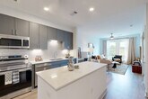 Located at 7400 S Addison Ct in Aurora, CO, this thoughtfully designed one-bedroom, one-bathroom residence offers a modern, open-concept floor plan on a single level. The combined dining, kitchen, and living area serves as the heart of the home, featuring light hardwood-style flooring that flows throughout. The kitchen is outfitted with sleek gray cabinetry, a white quartz waterfall island, white subway tile backsplash, stainless steel appliances including a range, microwave, dishwasher, and refrigerator, plus a dedicated pantry for added storage. Recessed lighting illuminates the space efficiently. The living area is bright and welcoming, highlighted by large windows that bring in natural light and frame outdoor views of the surrounding landscape. The bedroom includes a ceiling fan and direct access to the full bathroom, which features large-format marble-style tile surrounding a soaking tub and shower. A spacious walk-in closet with built-in shelving and hanging rods offers generous storage. Additional conveniences include an in-unit laundry area and a utility room. The entrance is accented with a stylish arched mirror, offering a polished first impression upon arrival.