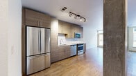 Located at 1910 S Josephine St in Denver, CO, this thoughtfully designed unit offers a modern, efficient layout across a single floor. The open-concept living area features light hardwood flooring throughout, large windows that invite abundant natural light, and a ceiling fan that enhances airflow and comfort. A glass door leads directly to a private balcony, providing outdoor access with views of the surrounding neighborhood.

The contemporary kitchen is well-appointed with flat-front wood-toned cabinetry extending to the ceiling for maximum storage, a white subway tile backsplash, and a full suite of stainless steel appliances including a refrigerator, range, microwave, and dishwasher. Track lighting overhead adds a clean, modern touch.

A hallway connects the living space to the remainder of the unit, lined with multiple closets offering generous storage solutions. The bathroom features a modern vanity with a white quartz countertop, wood-toned cabinetry, a large mirror, and tile flooring. An adjoining walk-in closet provides additional organizational space. In-unit laundry adds everyday convenience. Exposed concrete accent columns throughout lend an industrial character that complements the unit's contemporary aesthetic.