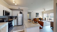 This single-floor residence offers a thoughtfully designed open-concept layout that seamlessly connects the kitchen, dining, and living areas. The kitchen is a functional centerpiece, outfitted with white cabinetry, granite-style countertops, a gray subway tile backsplash, stainless steel appliances including a refrigerator and range, and a spacious island that doubles as a breakfast bar. Crown molding adds a refined touch throughout the main living spaces.

The living room is bright and inviting, featuring wood-look flooring, crown molding, a ceiling fan, and a large sliding glass door that opens to an outdoor balcony, filling the space with natural light. A hallway connects the private areas of the home, leading to two comfortable bedrooms, each carpeted and equipped with ceiling fans. One bedroom benefits from large windows that invite ample daylight, while the other offers a cozy, warmly lit atmosphere.

A dedicated nook with mirrored walls and natural light from dual windows serves well as a home office or vanity space. The bathroom is clean and classic, featuring white cabinetry, a well-lit vanity mirror, and a full tub-shower combination with white tile surround. Light wood-tone flooring runs consistently through the common areas, tying the home's aesthetic together cohesively.