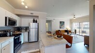 This single-floor residence offers a thoughtfully designed open-concept layout that seamlessly connects the kitchen, dining, and living areas. The kitchen is a functional centerpiece, outfitted with white cabinetry, granite-style countertops, a gray subway tile backsplash, stainless steel appliances including a refrigerator and range, and a spacious island that doubles as a breakfast bar. Crown molding adds a refined touch throughout the main living spaces.

The living room is bright and inviting, featuring wood-look flooring, crown molding, a ceiling fan, and a large sliding glass door that opens to an outdoor balcony, filling the space with natural light. A hallway connects the private areas of the home, leading to two comfortable bedrooms, each carpeted and equipped with ceiling fans. One bedroom benefits from large windows that invite ample daylight, while the other offers a cozy, warmly lit atmosphere.

A dedicated nook with mirrored walls and natural light from dual windows serves well as a home office or vanity space. The bathroom is clean and classic, featuring white cabinetry, a well-lit vanity mirror, and a full tub-shower combination with white tile surround. Light wood-tone flooring runs consistently through the common areas, tying the home's aesthetic together cohesively.