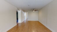 Located at 135 Sharene Ln in Walnut Creek, California, this single-floor residence offers a clean, functional layout with a cohesive neutral palette and wood-look flooring carried consistently throughout the space. The main living area is open and well-proportioned, featuring a ceiling fan with light fixture and a textured ceiling. Ample wall space provides flexibility for furniture arrangements, while the adjoining hallway connects the living zones to the private areas of the home. A bedroom with a sliding window allows natural light to filter in, offering a view of the surrounding greenery outside. A second room features plantation shutters that provide both privacy and light control, along with a wall-mounted air conditioning unit for individualized comfort. The kitchen is outfitted with white cabinetry, white countertops, and a full suite of white appliances including a refrigerator, electric range, built-in microwave, and dishwasher — providing a bright and practical cooking space. The bathroom includes a combined shower and tub, a toilet, and a vanity, finished in clean white tones with wood-look flooring that mirrors the rest of the home. Overall, the space presents a straightforward, well-maintained interior suited for comfortable everyday living in the heart of Walnut Creek.