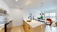 Located at 1240-1250 Cummings Ave in Ottawa, this thoughtfully designed one-bedroom, one-bathroom unit offers a modern open-concept layout with contemporary finishes throughout. Light hardwood flooring flows seamlessly across the entire space, complementing the crisp white walls and clean aesthetic.

The kitchen is a standout feature, equipped with warm wood cabinetry paired with white upper cabinets, a white quartz countertop island with a brass undermount sink and matte black faucet, a white tile backsplash, and stainless steel appliances including a refrigerator, stove, and microwave. The island doubles as a breakfast bar with seating. The adjacent dining area accommodates a round marble-top table beneath a sculptural pendant light, with a clear sightline into the kitchen.

The living room is bathed in natural light from large floor-to-ceiling sliding glass doors that open to a balcony, offering sweeping panoramic views of the Ottawa cityscape. The bedroom continues this connection to the outdoors, also featuring a large window with the same expansive city views.

The bathroom is elegantly finished with marble-look tile flooring, a sleek white floating vanity with gold accents, a large mirror, and a glass-enclosed walk-in shower with neutral tile surround. A dedicated closet provides practical storage.