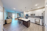 Located on Sunset Lake Dr in Shiloh, IL, this thoughtfully designed 2-bedroom, 2-bathroom residence offers a functional and modern living experience across a single floor. The open-concept kitchen and living area serves as the heart of the home, featuring luxury vinyl plank flooring throughout. The kitchen is outfitted with crisp white shaker cabinetry, a grey subway tile backsplash, quartz countertops, stainless steel appliances, pendant lighting, and a central island with bar seating — ideal for both cooking and casual dining. The living room flows seamlessly from the kitchen and is bathed in natural light from large floor-to-ceiling windows and sliding glass doors that open to a private balcony with outdoor views. The spacious primary bedroom includes a ceiling fan and direct access to a walk-in closet with built-in wire shelving. The second bedroom, also featuring a ceiling fan, offers comfortable proportions with its own closet. Both bathrooms are finished with white vanities, large mirrors, and wood-look flooring; one includes a full soaking tub and shower combo. A dedicated entrance and hallway provide a clean transition between spaces. The warm, neutral color palette and consistent finishes throughout create a cohesive and inviting atmosphere.