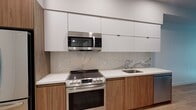Located at 1738 N Las Palmas Ave in Los Angeles, this single-floor unit showcases a clean, contemporary design throughout. The kitchen is a standout feature, outfitted with two-tone cabinetry — flat-panel white upper cabinets paired with warm wood-grain lower cabinets — complemented by white quartz countertops and a marble-style backsplash. Stainless steel appliances, including a range, over-the-range microwave, dishwasher, and refrigerator, complete the space. Light hardwood-style flooring extends throughout, unifying the kitchen with the open living area, which benefits from recessed lighting and access to a private outdoor space via French doors. The bedroom is bright and airy, featuring a tall window that brings in natural light and views of the surrounding neighborhood. The bathroom is finished with large-format tile flooring, a wood-vanity with white quartz countertop, an undermount sink, and a generously sized LED-backlit mirror, lending a sleek, modern feel. Overall, the unit offers a cohesive, contemporary aesthetic with quality finishes in the heart of Hollywood.