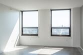 This single-floor unit presents a clean, contemporary aesthetic defined by polished terrazzo flooring that runs throughout, crisp white walls, and dark-finished doors that provide a striking visual contrast. The open living area is generously proportioned, bathed in natural light from large, black-framed windows that frame expansive city views, giving the space an airy, urban feel.

The kitchen is thoughtfully designed with rich dark cabinetry, granite countertops, and stainless steel appliances including a dishwasher, offering both style and functionality. A pass-through layout connects the kitchen seamlessly to the main living area.

The unit includes two well-appointed bathrooms. The first features a glass-enclosed walk-in shower with full tile surround, a built-in bench, and accessibility grab bars. The second bathroom offers a soaking tub and shower combination, a dark wood vanity with granite countertop, and a large mirror. Both bathrooms continue the terrazzo flooring found throughout the unit.

Additional rooms provide flexible living space, each with clean lines, bright white walls, and dark interior doors. The overall ambiance is modern and minimal, with an emphasis on durable, high-quality finishes and abundant natural light.