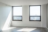 This single-floor unit presents a clean, contemporary aesthetic defined by polished terrazzo flooring that runs throughout, crisp white walls, and dark-finished doors that provide a striking visual contrast. The open living area is generously proportioned, bathed in natural light from large, black-framed windows that frame expansive city views, giving the space an airy, urban feel.

The kitchen is thoughtfully designed with rich dark cabinetry, granite countertops, and stainless steel appliances including a dishwasher, offering both style and functionality. A pass-through layout connects the kitchen seamlessly to the main living area.

The unit includes two well-appointed bathrooms. The first features a glass-enclosed walk-in shower with full tile surround, a built-in bench, and accessibility grab bars. The second bathroom offers a soaking tub and shower combination, a dark wood vanity with granite countertop, and a large mirror. Both bathrooms continue the terrazzo flooring found throughout the unit.

Additional rooms provide flexible living space, each with clean lines, bright white walls, and dark interior doors. The overall ambiance is modern and minimal, with an emphasis on durable, high-quality finishes and abundant natural light.