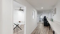Located at 2353 Portland St in Los Angeles, CA, this single-floor space offers a clean, minimalist layout designed for functional, communal use. The interior is finished throughout with light wood-look flooring and crisp white walls, creating a bright and cohesive atmosphere.

The hallway entrance features recessed lighting and a large cork bulletin board, providing a practical area for announcements and information sharing. A built-in countertop shelf runs along one wall, offering additional workspace or display space.

The main living area is thoughtfully appointed with multiple functional zones. A wall-mounted flat-screen television anchors the lounge area, complemented by a plush sofa and a low coffee table. Adjacent to this is a utility nook equipped with a coffee machine, mini-refrigerator, and a water dispenser, making the space well-suited for extended use. A long, wall-spanning built-in shelf with black metal legs provides generous workspace, with a wall-mounted AC unit overhead for climate control.

A separate enclosed room—accessible via a frosted glass-panel door—serves as a private meeting or office area, furnished with a glass-top table, leather chair, wall-mounted TV, and a glass whiteboard, ideal for focused work or small group meetings. A door from this room leads directly outside. The space also provides access to a laundry room.