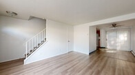 This two-floor residence offers a straightforward and functional layout designed for comfortable everyday living. The main level features light-toned wood laminate flooring throughout the open living areas, crisp white walls, and a staircase with white railings connecting to the upper floor. The living space is well-lit, with a ceiling fan and large windows fitted with vertical blinds allowing natural light to fill the room. Baseboard heating units are present throughout, ensuring warmth across both levels. The kitchen is equipped with dark wood cabinetry, granite-style countertops, a black electric range, and an over-the-range microwave, providing a compact and efficient cooking space. Two bathrooms serve the home — one featuring full-wall tile surround, a soaking tub with shower, a window for natural light, and tile flooring, while the second is a simpler half-bath with tile flooring. The upper level hosts carpeted bedrooms with neutral tones, each offering built-in closet storage with bifold doors. The bedrooms provide a quiet retreat, with baseboard heating and ample wall space. Overall, the space presents a clean, move-in ready environment with practical finishes throughout.