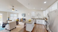 This well-appointed single-floor residence offers a thoughtfully designed open-concept layout that seamlessly connects the kitchen, dining, and living areas. The kitchen is a standout feature, showcasing crisp white shaker cabinetry, taupe quartz countertops, stainless steel appliances including a refrigerator, range, microwave, and dishwasher, and a central island with bar seating — all set atop warm hardwood flooring. The adjoining living room benefits from soaring vaulted ceilings, a ceiling fan, and generous natural light streaming through multiple windows and a sliding glass door that opens onto a private balcony with outdoor seating.

The bedrooms are comfortably sized, each featuring plush carpeting, ceiling fans, and windows that invite natural light. The primary bedroom offers ample space for a large bed and dresser. A full bathroom includes a tub-shower combination, hardwood flooring, white cabinetry, and recessed lighting. A dedicated office or flex room rounds out the layout, offering carpeted flooring, a large window, and enough space for a full workstation. Throughout the home, a neutral color palette and clean finishes create a bright, cohesive, and welcoming atmosphere.