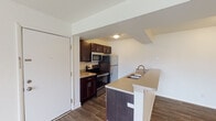 This single-floor unit on Thomas Court in Portage, Michigan, offers a thoughtfully designed open-concept layout that seamlessly connects the kitchen and living areas. The kitchen is equipped with stainless steel appliances, including a refrigerator, range, and microwave, complemented by rich dark cabinetry and light-toned countertops. A peninsula with a built-in sink and additional counter space extends into the main living area, providing both functional workspace and a natural division between cooking and living zones.

The living area is generously sized, featuring durable wood-style plank flooring that runs throughout the main space, contributing to a clean and cohesive aesthetic. White walls and neutral tones keep the interior bright and versatile. A sliding glass door with vertical blinds opens to an outdoor area, allowing natural light to flow into the room. Ceiling vents indicate a central HVAC system for year-round climate control.

The bedroom offers a quieter retreat, finished with wall-to-wall carpet for added comfort and a window with a view of the surrounding greenery. The overall design balances practicality with a clean, modern sensibility suited for everyday living.