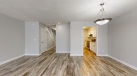 Located at 406 E Broad St in Newnan, Georgia, this two-story space presents a clean, contemporary interior with a neutral gray and white color palette throughout. The main level opens to a spacious living area finished with wood-look luxury vinyl plank flooring and a textured ceiling. A pendant light fixture adds a decorative touch, while a staircase connects to the upper level. French doors and multiple windows allow natural light to flow into the generously sized living room, which also features a ceiling fan.

The galley-style kitchen is well-appointed with white shaker cabinetry, light granite-style countertops, stainless steel and black appliances, and matching wood-look flooring. An open pass-through connects the kitchen visually to the main living and dining areas.

Bedrooms are found across both floors, with wood-look or carpeted flooring depending on the room. Each bedroom is served by a bathroom featuring white vanity cabinetry, white countertops, and tub-shower combinations. One bathroom includes direct access to a walk-in closet outfitted with built-in wire shelving, offering practical storage solutions. The overall design is cohesive, functional, and move-in ready.