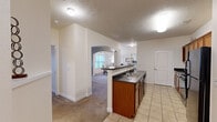 Located at Copper Chase in Greenwood, Indiana, this single-floor, three-bedroom, two-bathroom home offers a well-organized layout designed for comfortable everyday living. The galley-style kitchen is equipped with dark countertops, warm wood cabinetry, black appliances including a range, microwave, refrigerator, and dishwasher, and light tile flooring that extends through the main corridors. A pass-through window connects the kitchen to the adjacent dining area, which features a pendant light fixture and a bright window dressed with sheer curtains, allowing natural light to fill the space. The living room offers crown molding, neutral tones, plush carpeting, and a glass-panel door that opens to the outdoors, adding both light and accessibility. The dining room is carpeted and sized for a standard dining set. The primary bedroom is a comfortable retreat with carpeted floors, arched doorways, and access to a well-organized walk-in closet outfitted with multi-tier wire shelving. The bathrooms include a full tub-shower combination with white tile surround and built-in corner shelving. A dedicated laundry room with wire shelving and washer hookup adds in-unit convenience. Textured ceilings and consistent neutral wall tones are found throughout, creating a cohesive and clean aesthetic across the entire home.