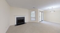 This single-floor, 2-bedroom, 2-bathroom home in Columbus, GA offers a functional and comfortable layout designed to maximize everyday living. The living room serves as the heart of the home, featuring a classic fireplace with a white mantle and dark surround, plush neutral carpeting, and sliding glass door access to the exterior, allowing for natural light throughout. The kitchen is open and well-appointed, with white cabinetry, a decorative diamond wine rack, light countertops, black appliances including a refrigerator and electric range, and a beadboard-paneled peninsula that connects to the living area. Hardwood flooring runs through the kitchen and bathrooms, adding warmth and continuity. Both bedrooms are carpeted, each equipped with a ceiling fan and windows with outdoor views, creating bright and airy retreats. The spacious primary bedroom includes its own dedicated closet space. Three closets in total provide generous storage, including a walk-in closet outfitted with multi-level wire shelving and a pantry-style closet in the kitchen area. Both bathrooms feature tub-shower combinations, white vanity cabinetry, and brushed nickel fixtures, maintaining a clean and consistent aesthetic throughout the home.