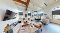 This 2-bedroom, 2-bathroom residence at The Mill showcases a striking blend of historic character and modern design across a single thoughtfully arranged floor. The open-concept living, dining, and kitchen area is the centerpiece of the home, defined by dramatically vaulted ceilings with exposed wooden beams and a row of signature arched windows that flood the space with abundant natural light and offer views of the surrounding greenery and waterway. Wide-plank hardwood flooring and crisp white walls create a clean, airy backdrop throughout. The living area accommodates generous seating and entertainment, while the dining zone and well-appointed kitchen flow seamlessly alongside it. The kitchen features light cabinetry, sleek countertops, and a window framing an idyllic outdoor view. Both bedrooms are comfortably sized, with the primary featuring a pair of arched windows, and both are served by their own full bathrooms — one with a glass-enclosed walk-in shower finished in stone-look tile, and the other with a tub/shower combination and a white vanity. A ceiling fan, pendant lighting, and curated vintage travel artwork add personality and warmth throughout, making this a distinctive and well-appointed residence within a converted mill building.