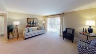 This single-floor, two-bedroom, one-bathroom residence offers a thoughtfully arranged layout that maximizes comfort and functionality. The spacious living room features plush wall-to-wall carpeting, warm neutral-toned walls, and a large sliding glass door that floods the space with natural light while providing access to the outdoors. The adjoining dining area makes a stylish statement with a contemporary sputnik chandelier overhead and a glass-top dining table, creating a distinct and memorable entertaining space. The kitchen is equipped with white cabinetry, ample counter space, a coil-top range, and a full-size refrigerator, offering a clean and efficient workspace. Both bedrooms are generously sized with soft carpeted floors and soothing gray-toned walls. The primary bedroom includes a mirrored sliding closet door, while the second bedroom offers comfortable proportions ideal for rest or a personal retreat. The full bathroom features a combined tub and shower with tile flooring, a white vanity, and open wall shelving for added storage. Throughout the residence, the consistent use of neutral palettes and carpet flooring creates a cohesive, calm ambiance well-suited for everyday living.