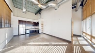 Located at 401 S Elgin Ave in Tulsa's dynamic Arts District, this 2-bedroom, 2-bathroom loft delivers a striking industrial aesthetic throughout. The open-plan living and kitchen area commands attention with soaring ceilings, exposed steel beams, and bold silver ductwork overhead, all anchored by polished concrete floors that run seamlessly through the space. Floor-to-ceiling windows flood the interior with natural light and offer views of the surrounding cityscape, while a sliding glass door provides direct outdoor access.

The well-appointed kitchen features rich dark cabinetry, granite countertops, stainless steel appliances including a refrigerator, range, microwave, and dishwasher, complemented by a pendant-lit island with matching granite surface — ideal for both cooking and casual dining.

The bedrooms continue the loft's industrial character, with painted brick walls, large windows, and polished concrete floors that maximize the sense of openness. Both bathrooms are finished with large-format tile flooring, tiled tub-shower surrounds with built-in niches, dark cabinetry, and granite vanity tops. A dedicated in-unit laundry area with a stacked washer and dryer adds everyday convenience to this urban retreat.