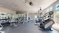 Located at 4363 S Quebec St in Denver, Colorado, this fitness center offers a spacious, well-organized workout facility spread across a single floor. The space is divided into distinct functional zones, each designed to support a variety of training styles and fitness goals.

The main workout area features a generous selection of cardio equipment, including treadmills, ellipticals, stair climbers, and stationary bikes, positioned to allow comfortable spacing between machines. Large windows along one wall flood the space with natural light and provide views of the surrounding area, enhancing the overall workout environment.

The strength training section is equipped with cable machines, a multi-station smith machine, weight benches, and a full rack of dumbbells. Full-length mirrors line portions of the walls, creating a sense of added depth while allowing users to monitor their form during exercises.

Overhead, industrial-style ceiling fans are mounted throughout to maintain air circulation, complementing the recessed lighting that keeps the space well-lit at all times. The durable rubber flooring provides both safety and comfort underfoot across all zones.

A separate alcove area features additional isolated strength machines set against a cool blue accent wall, offering a quieter space for targeted muscle training. The overall ambiance is clean, functional, and professional, making this fitness center a comprehensive resource for residents in the Denver area.